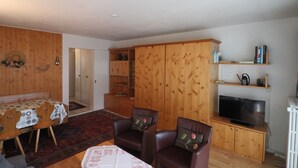Ein Wohnzimmer mit Holzschrank, Fernseher und einem Essbereich mit Tisch und Stühlen.