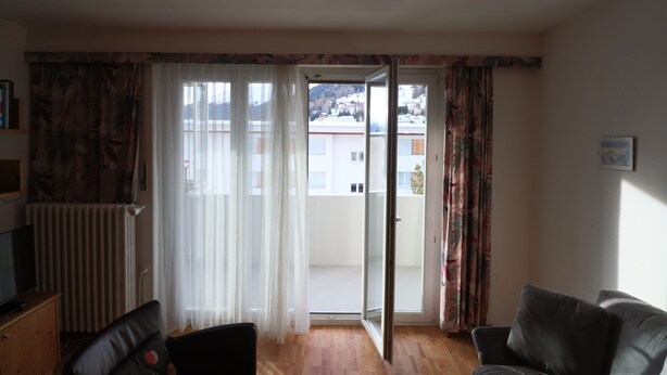 Ein Wohnzimmer mit einer Couch, einem Fernseher und einer Schiebetür zu einem Balkon.