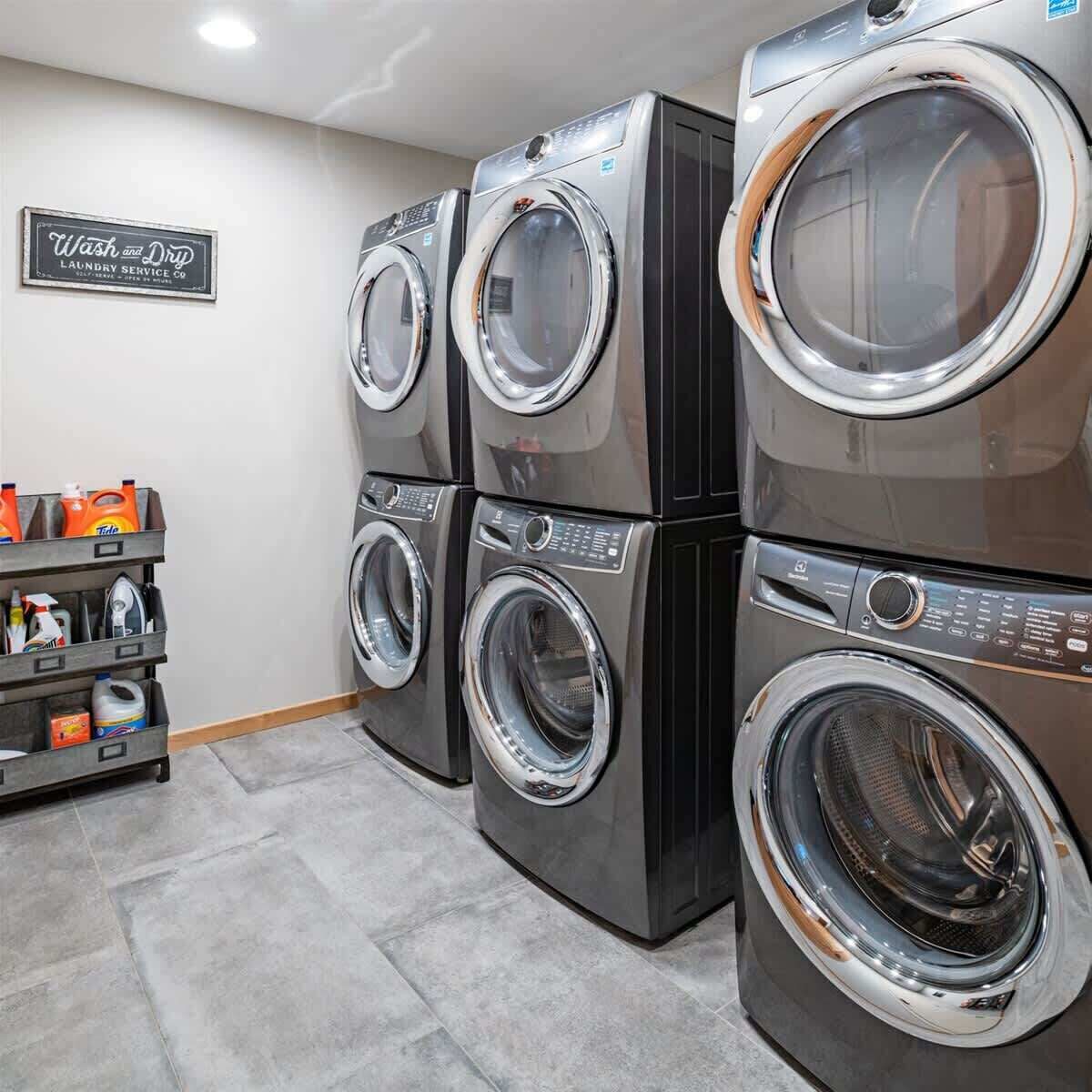 A laundry facility with stacked front-loading washers and dryers, a shelf with cleaning supplies, and a sign for 'Wash and Dry Laundry Service Co.'
