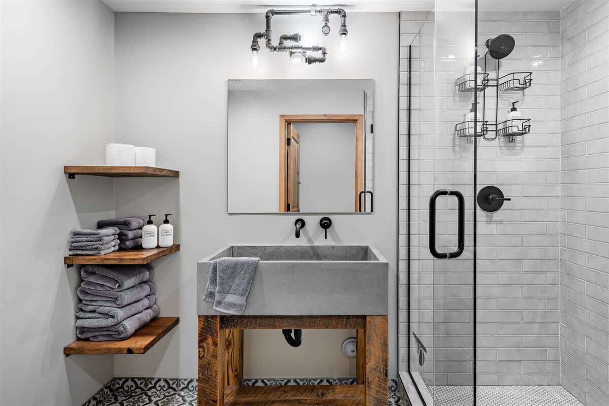 A modern bathroom with a grey sink, wooden shelves, a mirror, and a glass shower enclosure.