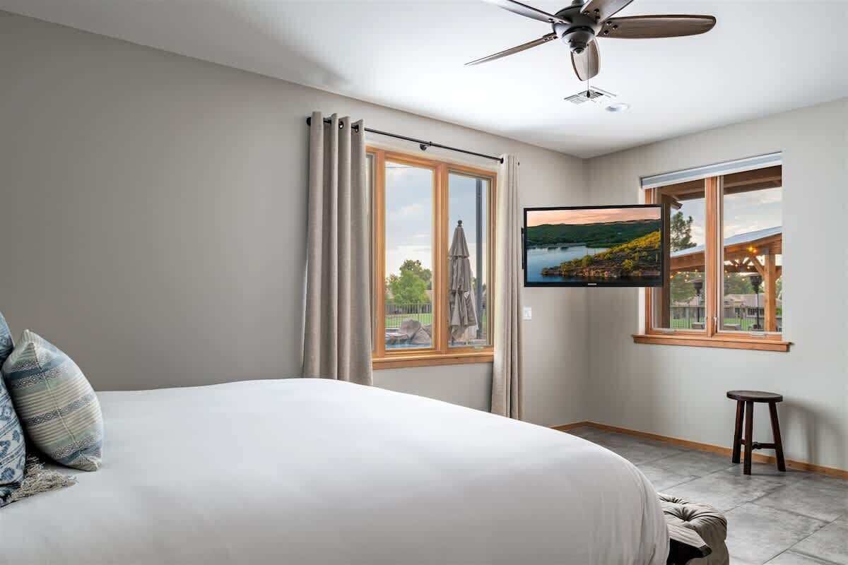 Una camera da letto con un letto, una TV a parete, una ventola a soffitto e una finestra con tende.