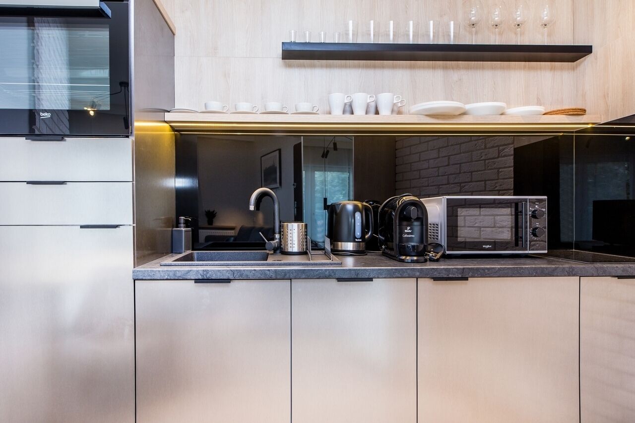 Una cocina moderna con microondas integrado, hervidor de agua y cafetera, encimera de madera y estante con tazas y platos.