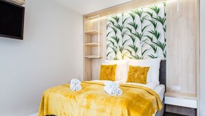 Une chambre d’hôtel moderne, équipée d’un lit, d’une étagère intégrée et d’un mur orné d’un motif de feuilles.