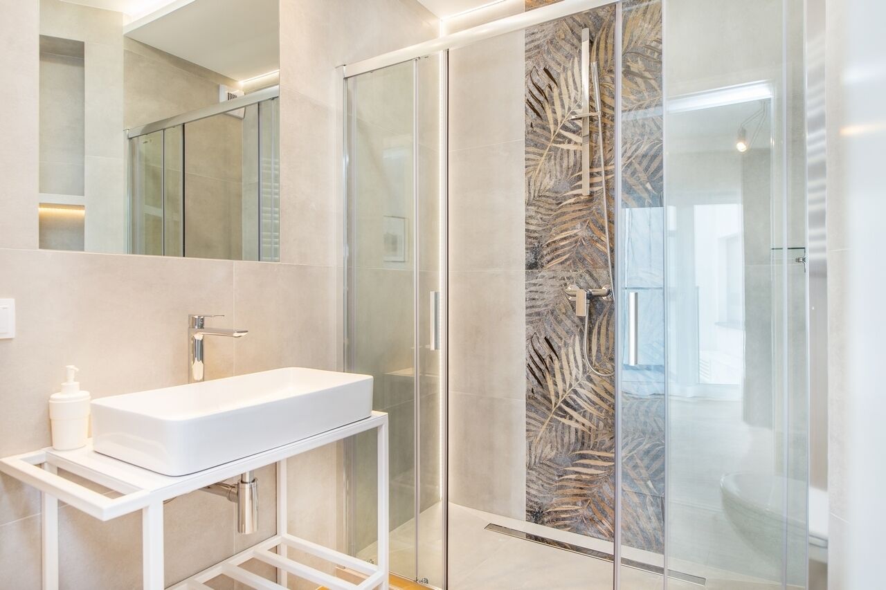 A modern bathroom with a glass shower enclosure, a white sink, and a marble backsplash.