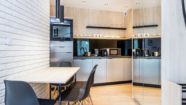 Une cuisine moderne avec un mur en briques, des appareils en acier inoxydable et un coin repas comprenant une table et des chaises.
