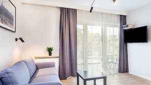 Un salon moderne avec un canapé gris, une petite table et un téléviseur fixé au mur.