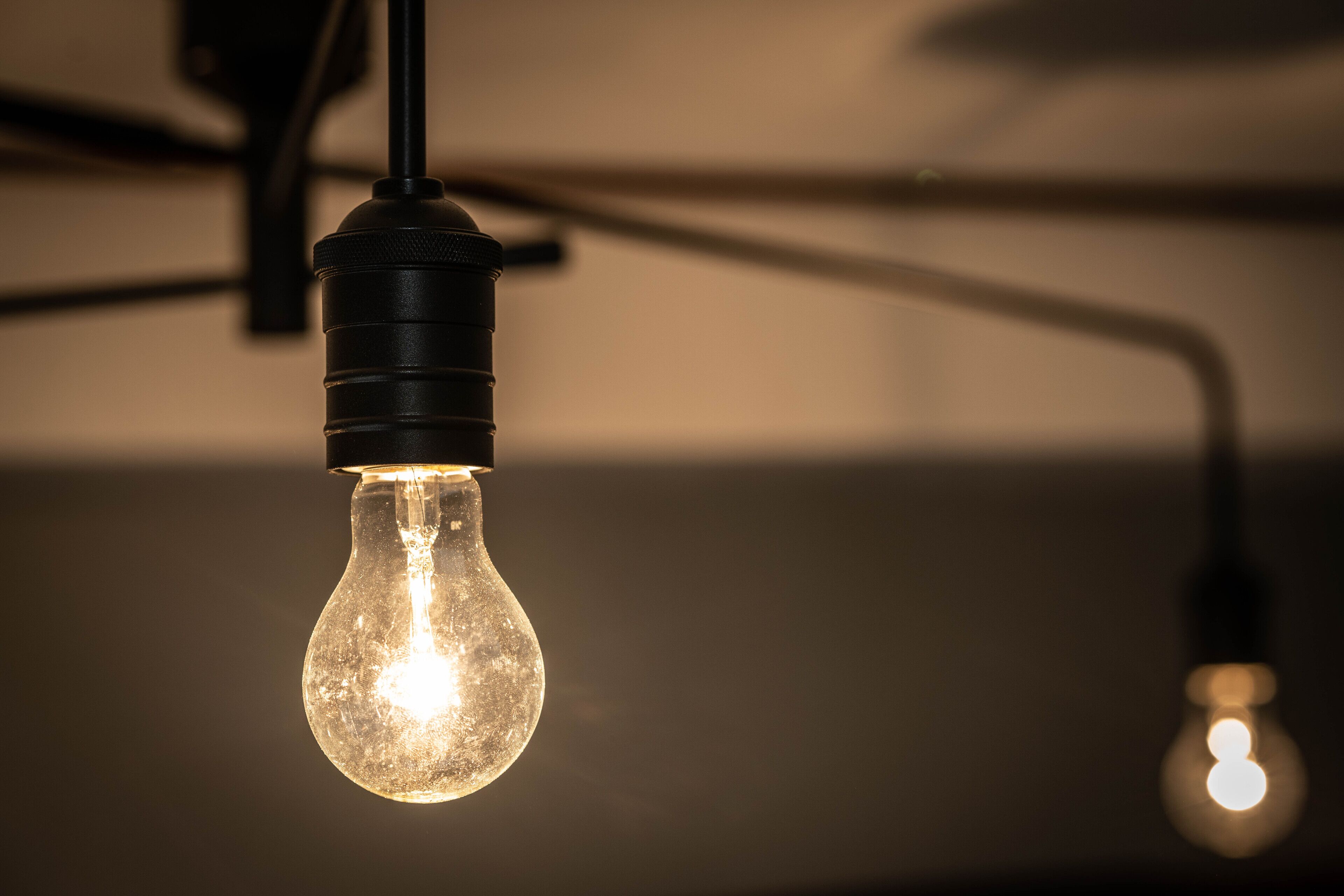 A close-up of a single light bulb with a visible filament, hanging from a black fixture.