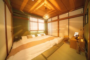 A traditional Japanese-style bedroom with tatami flooring, a large bed with white bedding, a shoji screen door, and a small desk with a lamp. - Fujimi Room (Tokyo)