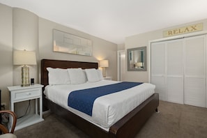 Une chambre d’hôtel bien rangée, avec un lit, des lampes de chevet, une table de chevet, une chaise, une armoire et une pancarte sur laquelle on peut lire « DÉTENTE ».