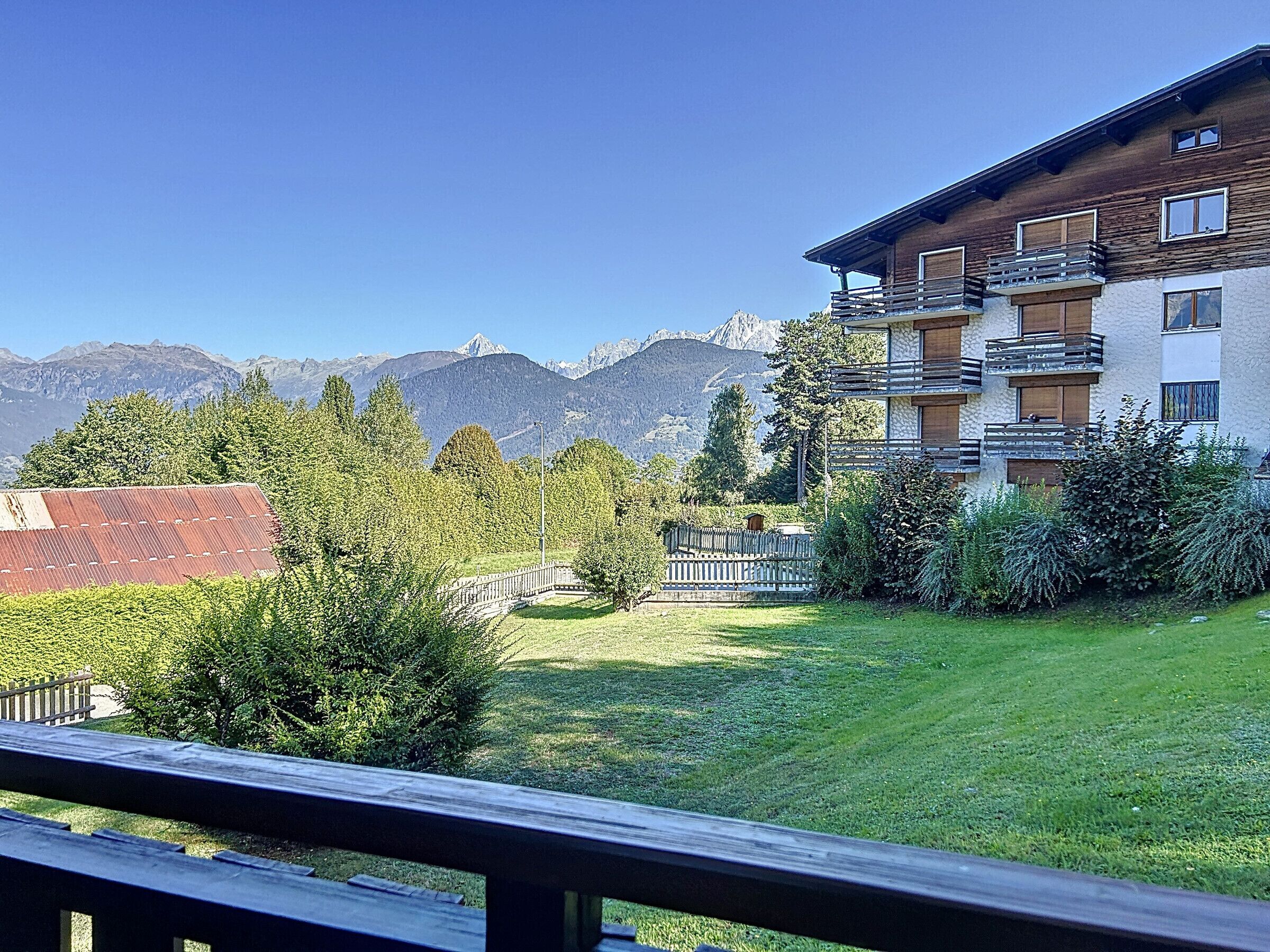 Un hôtel avec vue sur les montagnes, doté d’un balcon en bois, d’une pelouse verdoyante et offrant une vue dégagée sur les montagnes.
