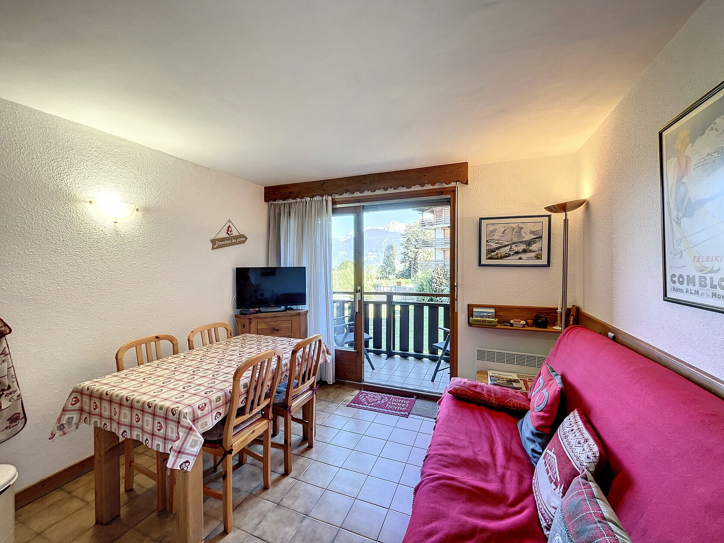 Un salon confortable avec un coin repas, un téléviseur et un balcon offrant une vue sur les montagnes.