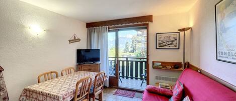 Un salon confortable avec un coin repas, un téléviseur et un balcon offrant une vue sur les montagnes.