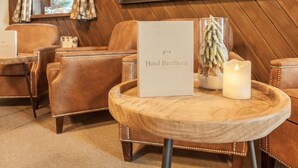 Un hall d’hôtel accueillant, avec des fauteuils en cuir, une petite table en bois sur laquelle repose un menu, une bougie allumée et un tableau encadré accroché au mur.