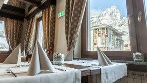 Un espace repas avec des tables préparées pour deux personnes, une vue sur une montagne et un panneau indiquant la sortie de secours.
