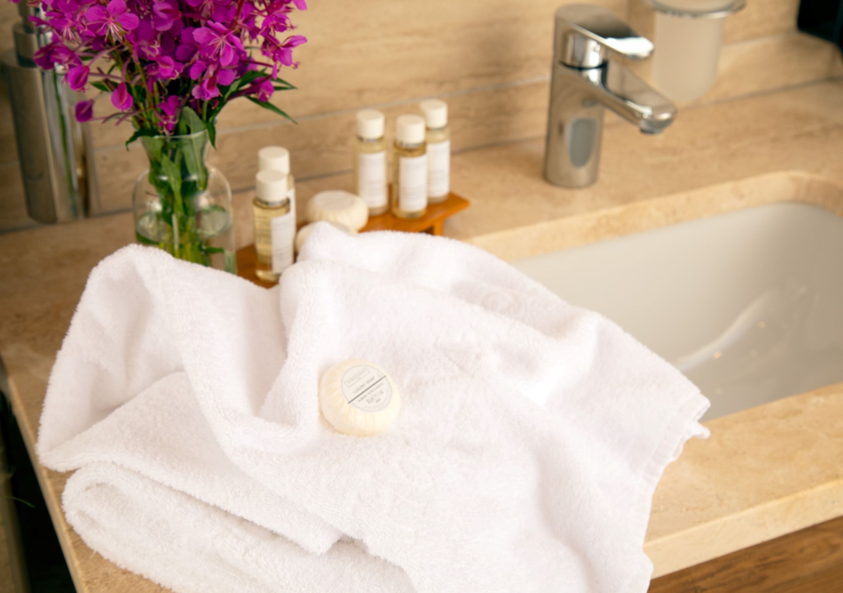 Un lavabo de salle de bain avec une serviette blanche, un savon et un vase rempli de fleurs violettes.