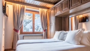 Une chambre d’hôtel avec un plafond en bois, une grande fenêtre avec des rideaux, un lit avec du linge de lit blanc et un téléviseur fixé au mur.