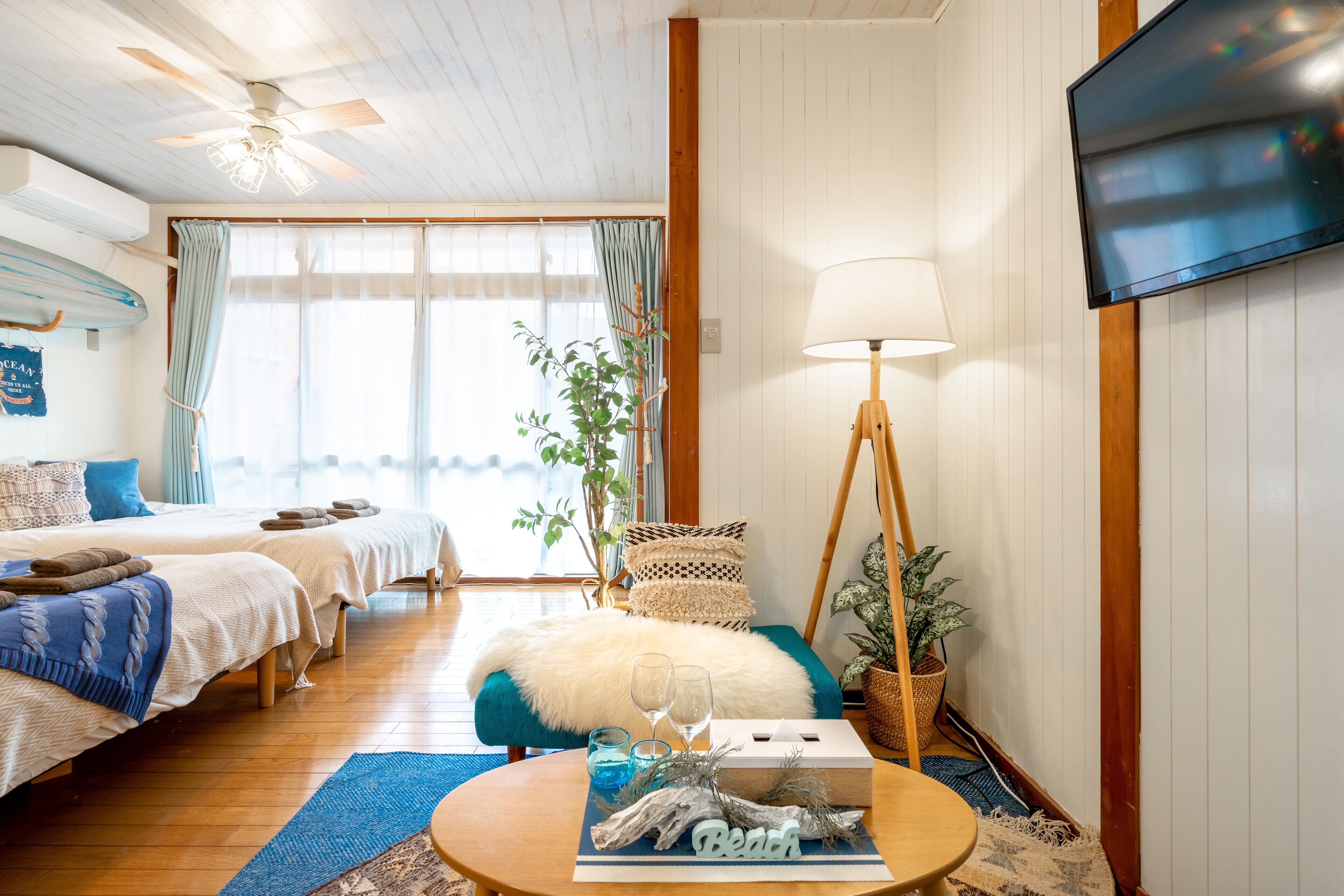 A cozy bedroom with two beds, a TV, a ceiling fan, and a window with curtains.