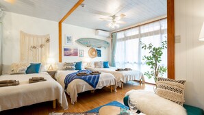 Una habitación acogedora con dos camas, un ventilador de techo, una decoración con tabla de surf y un ventanal con cortinas.