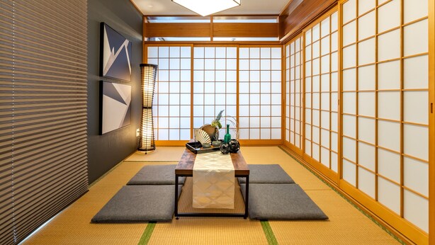 Una habitación japonesa tradicional con suelo de tatami, paneles shoji, una mesa baja con estera, y una lámpara colgante.