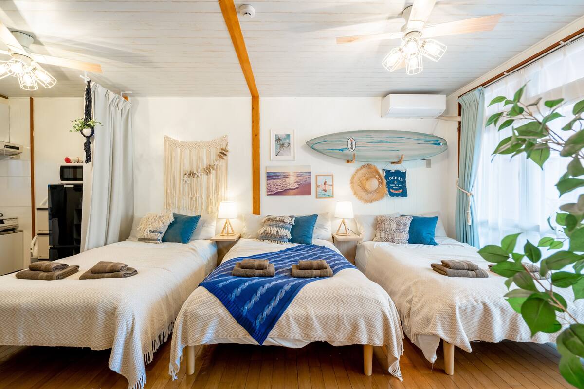 Habitación de hotel con dos camas, un ventanal grande y una tabla de surf en la pared.