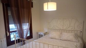 A bedroom with a bed, a bedside table, a window with curtains, and a hanging light fixture.