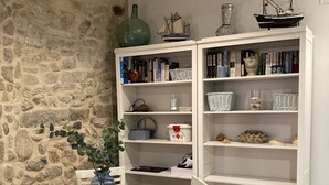 A dining area with a glass table, white chairs, a stone wall, and a white bookshelf filled with books and decorative items.