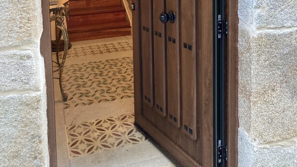 A wooden door with a geometric design and a small window, leading to a staircase with wooden steps and a patterned floor.