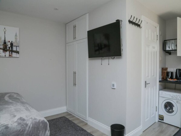 A bedroom with a bed, a wardrobe, a television, a washing machine, and a small kitchen area.