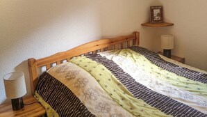 A bedroom with a wooden bed, a bedside lamp, a framed picture on a shelf, and a small potted plant. - 2-room cabin apartment at the foot of the slopes (Les Adrets-Prapoutel)
