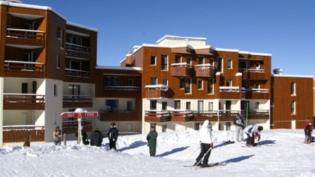 A multi-story building with balconies, a ski resort in the background, and people skiing. - 2-room cabin apartment at the foot of the slopes (Les Adrets-Prapoutel)