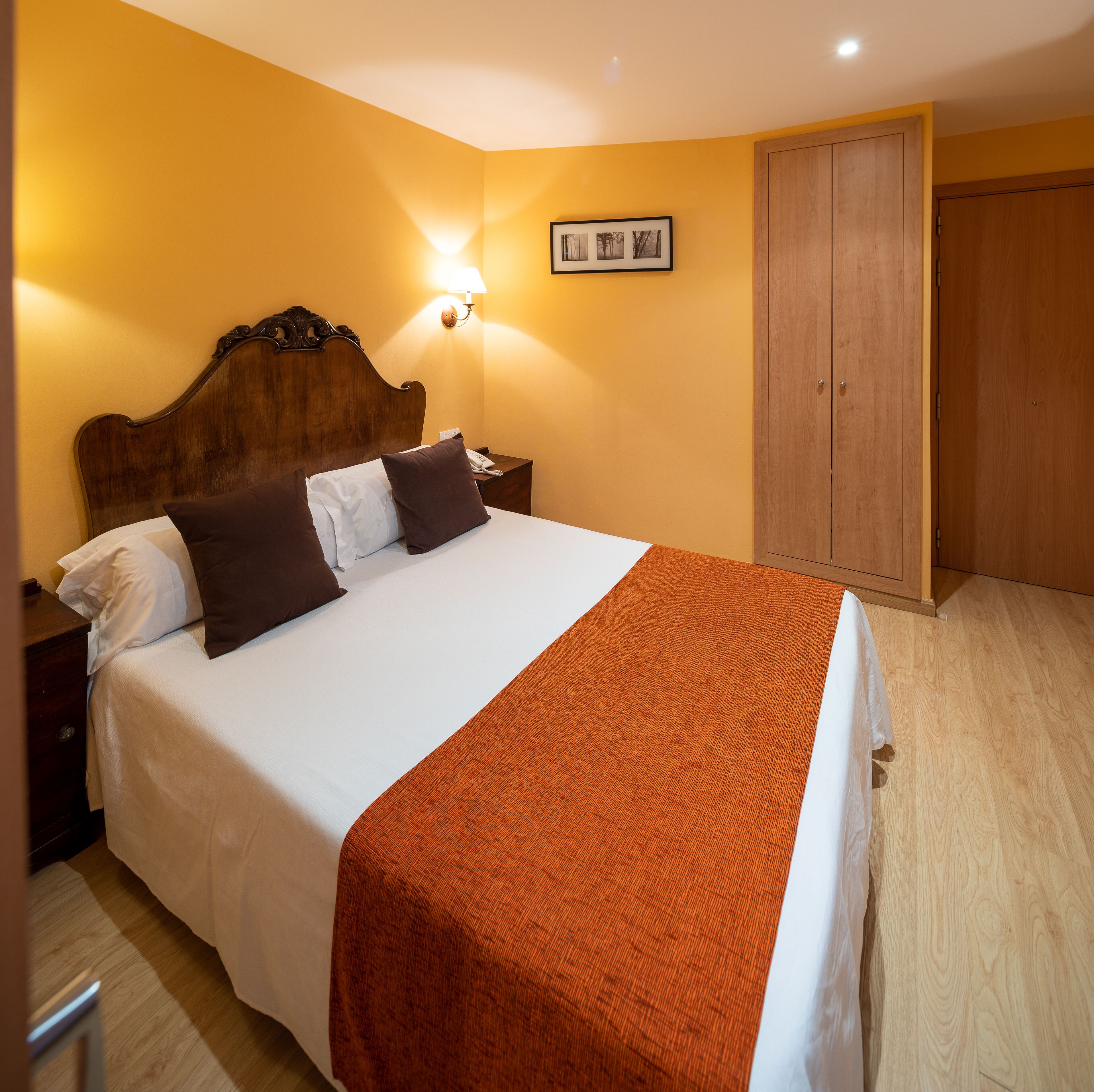 A neatly made bed with a white and brown blanket, a wooden headboard, and a nightstand with a lamp.