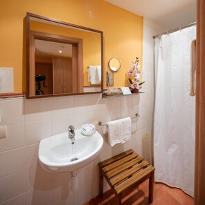 Un baño con lavamanos blanco, banco de madera y espejo sobre el lavamanos.