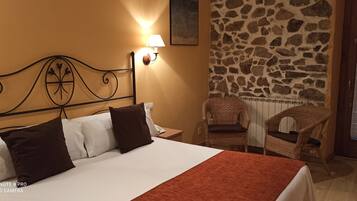Een hotelkamer met een bed, nachtkastje, lamp, een stenen muur en een rieten stoel.