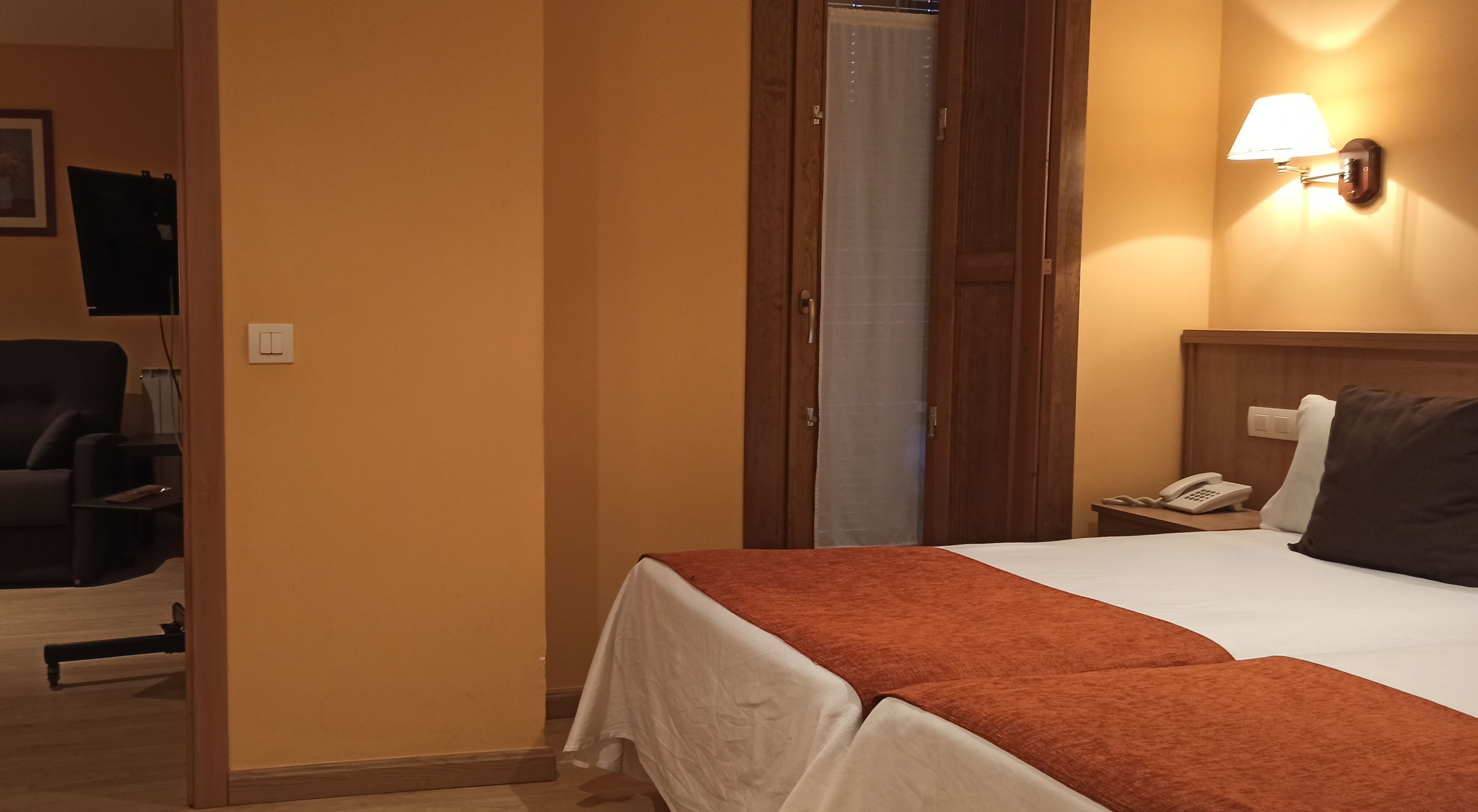 A hotel room with a bed, a nightstand, a phone, and a wall-mounted lamp.