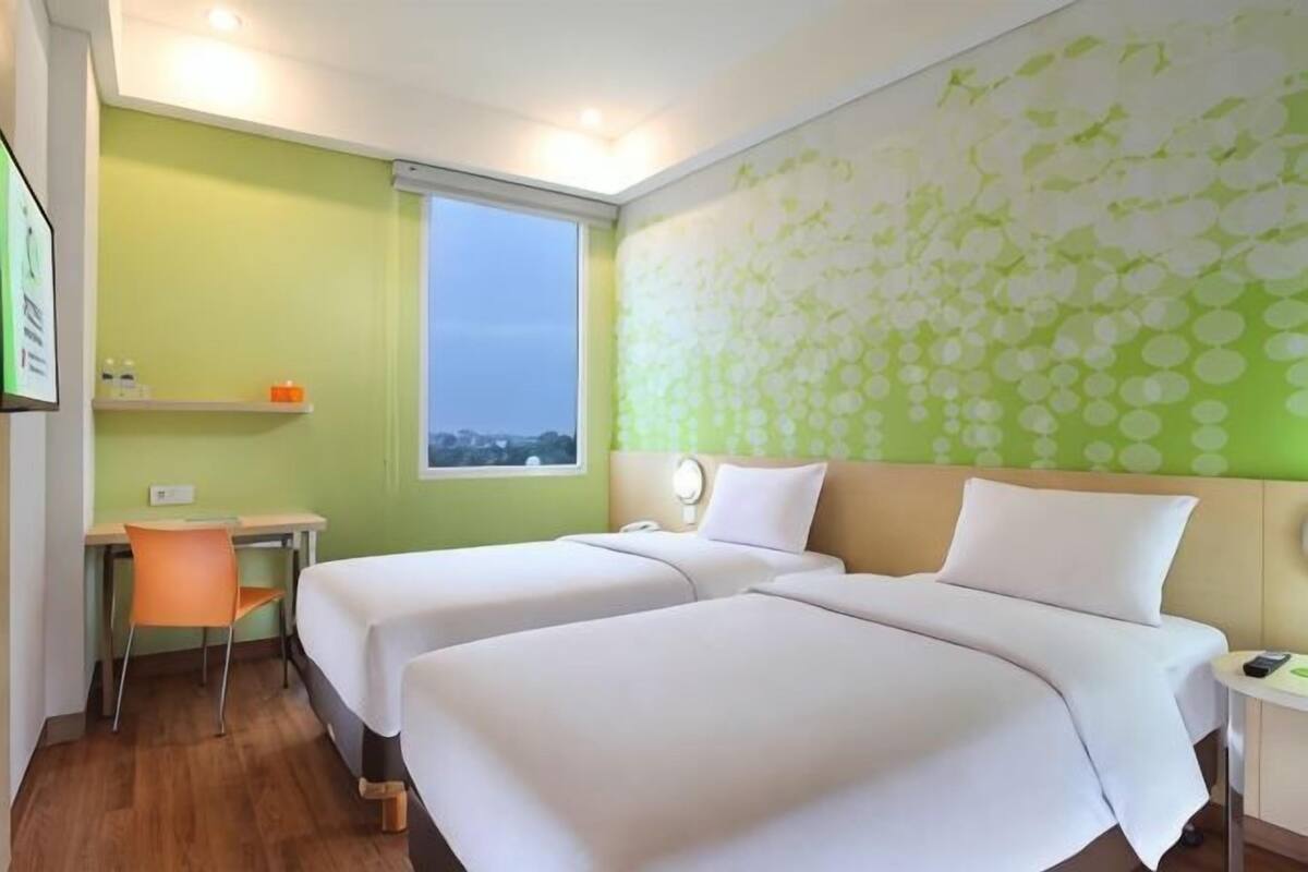 Hotellihuone, jossa on kaksi sänkyä, työpöytä, tuoli, pieni pöytä ja ikkuna.