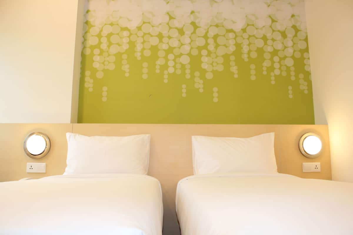 A hotel room with two beds, a green wall with a floral design, and round wall sconces.