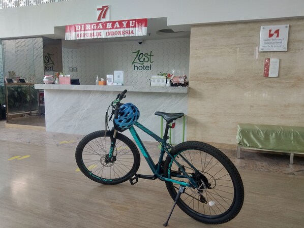 Un mostrador de recepción con un cartel que dice 'Dira Haya' y 'Lost Hotel'. Una bicicleta color turquesa con casco azul está estacionada al frente.