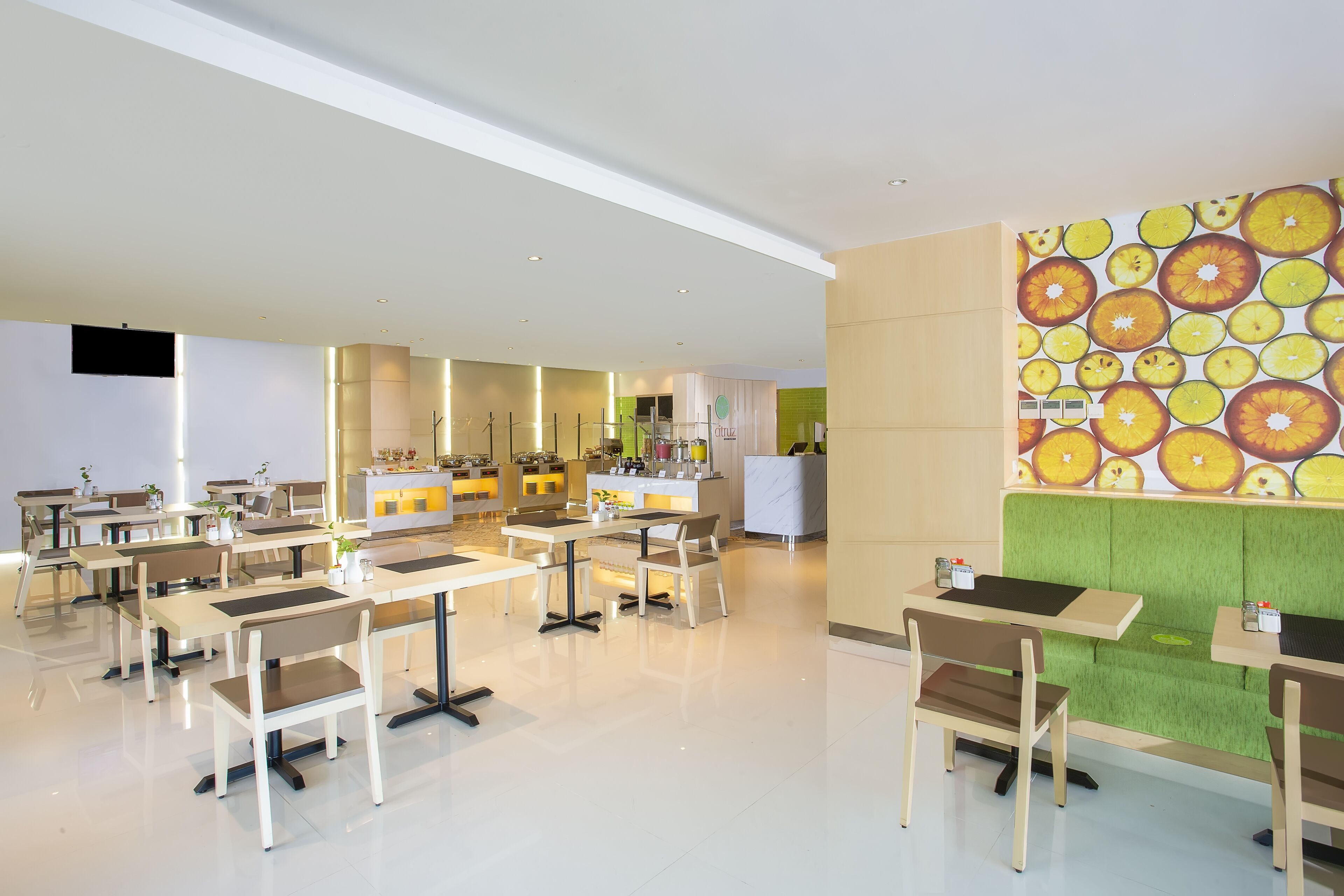 Un comedor moderno con varias mesas y sillas, una cocina al fondo y una pared vibrante decorada con fruta.
