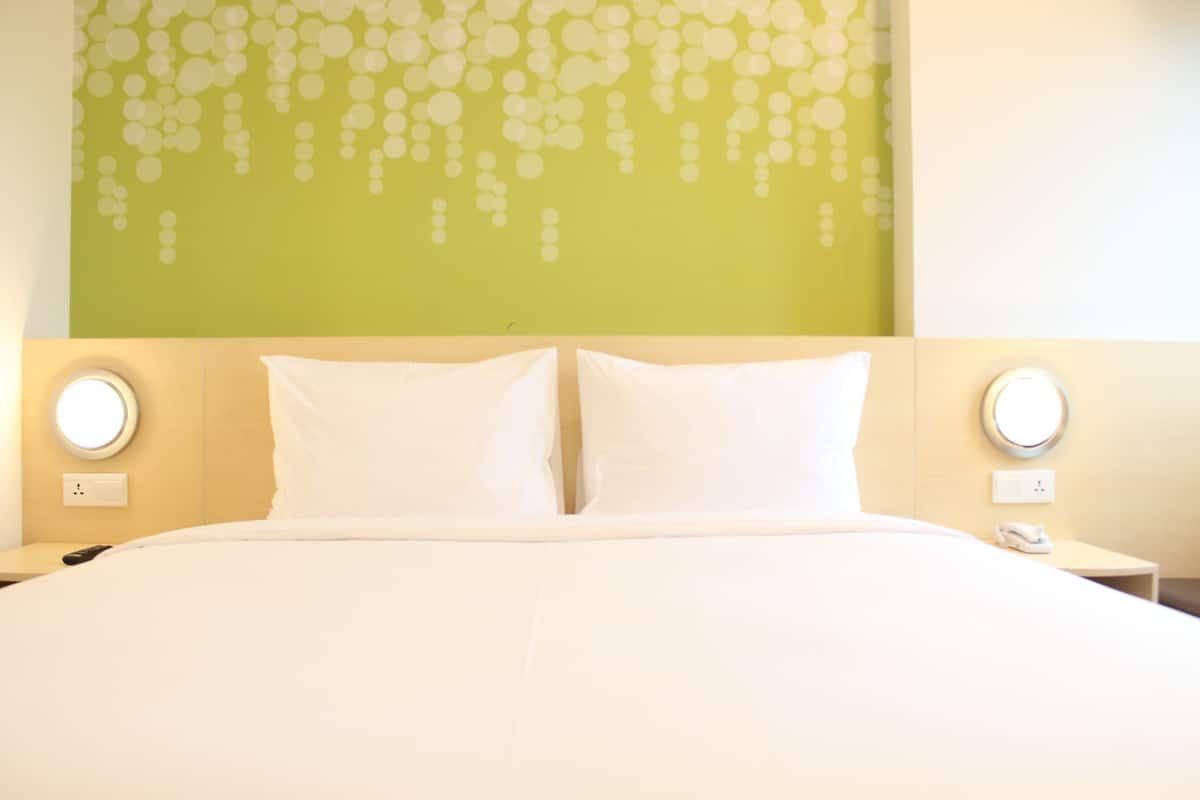 A hotel room with a large bed, two bedside tables, and a green wall with a circular pattern.