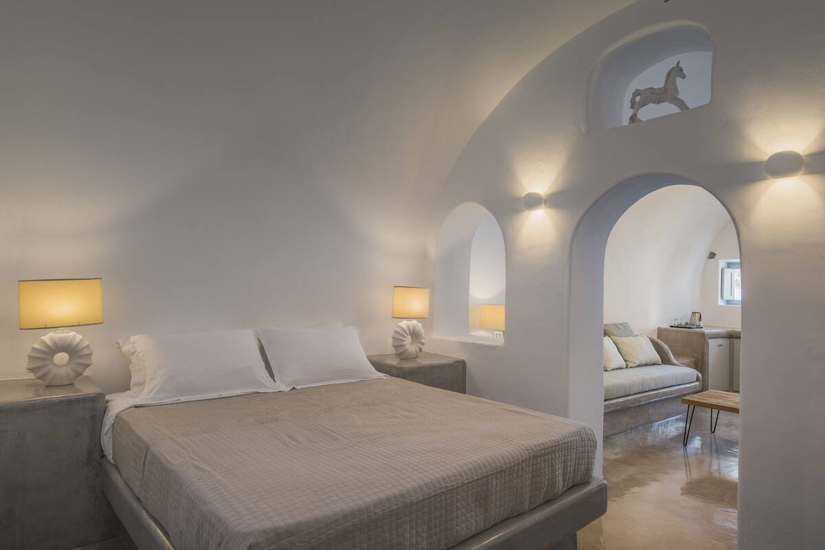 Un dormitorio con una cama grande, dos mesitas de noche con lámparas, un sofá y una pequeña mesa.