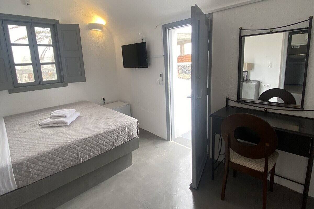 Un dormitorio con cama, escritorio, silla, televisor y puerta que da a un espacio exterior.