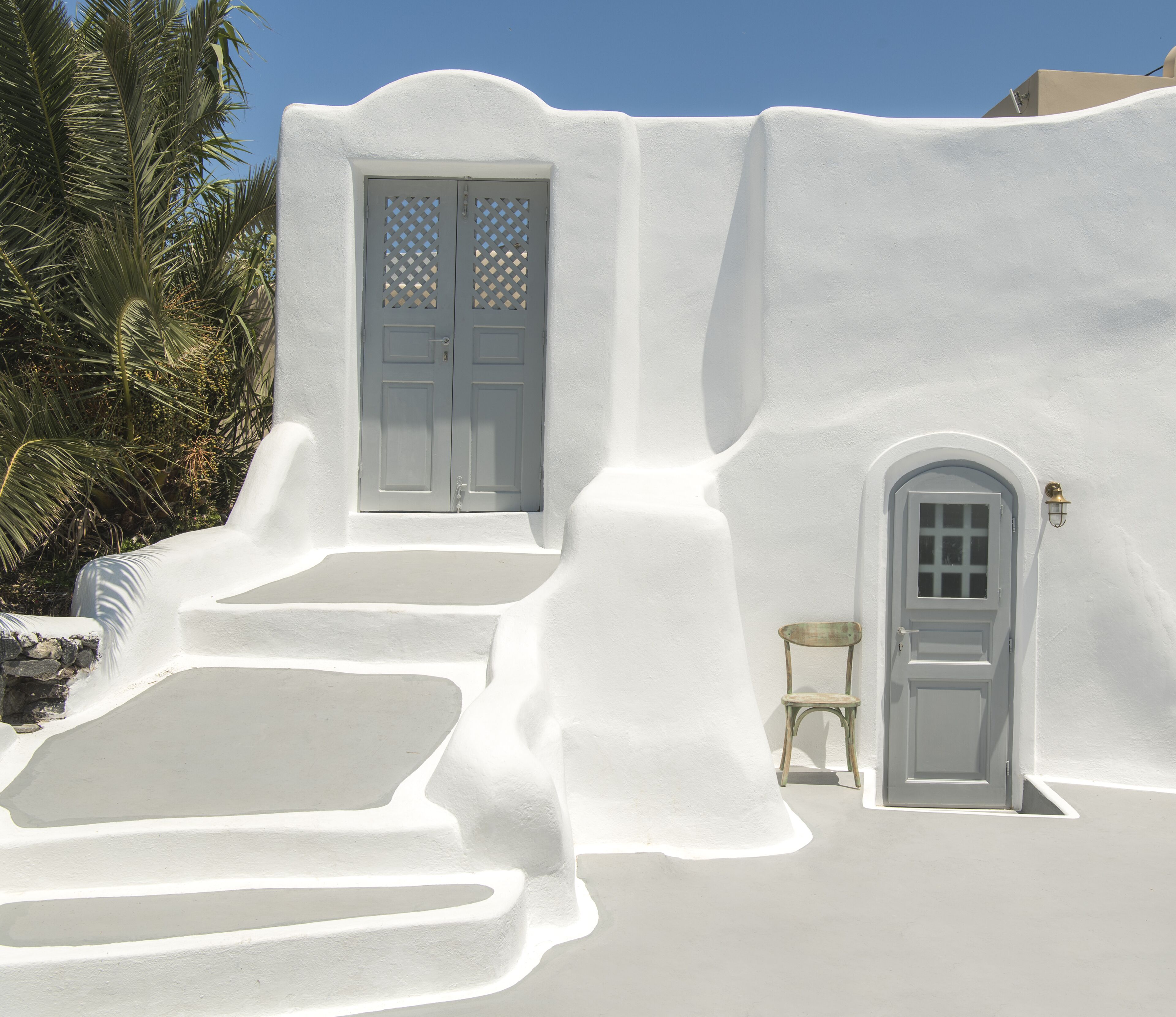 A white-washed building with a large door and a smaller door, both with simple designs.