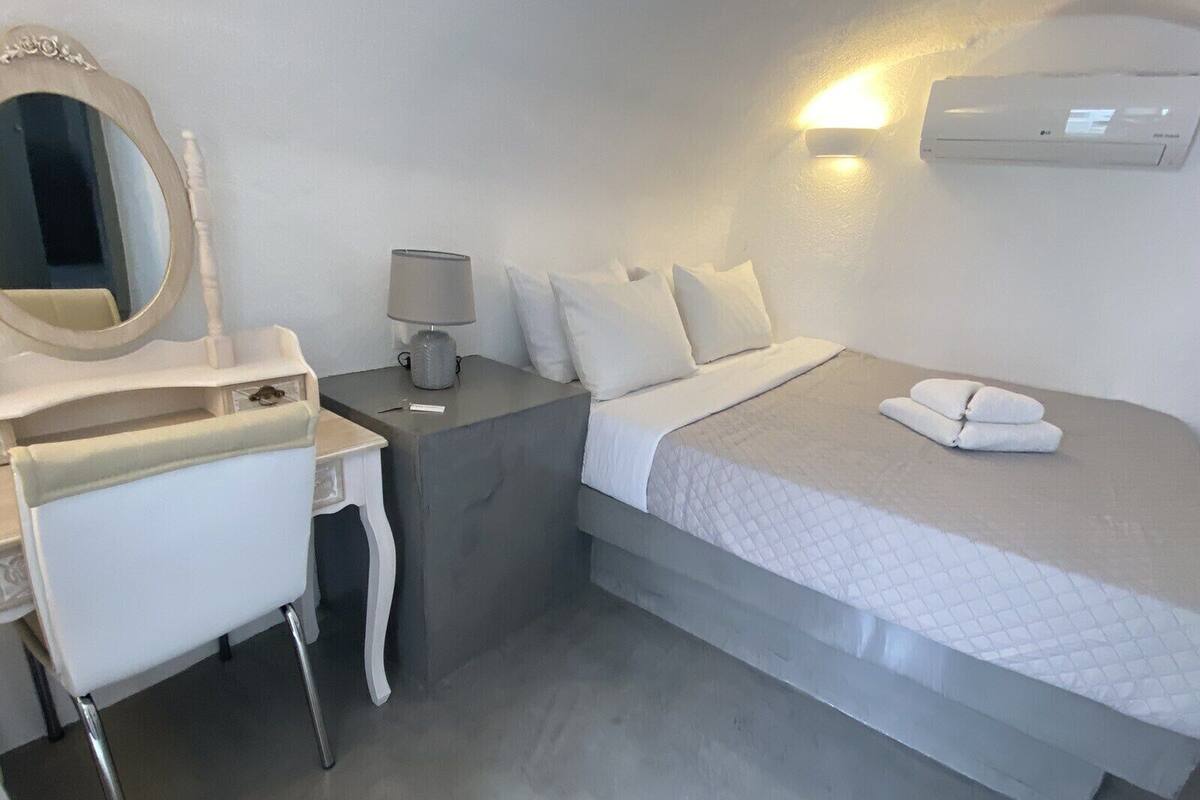Una habitación de hotel con una cama, una mesita de noche con lámpara, un tocador con espejo y un aire acondicionado instalado en la pared.