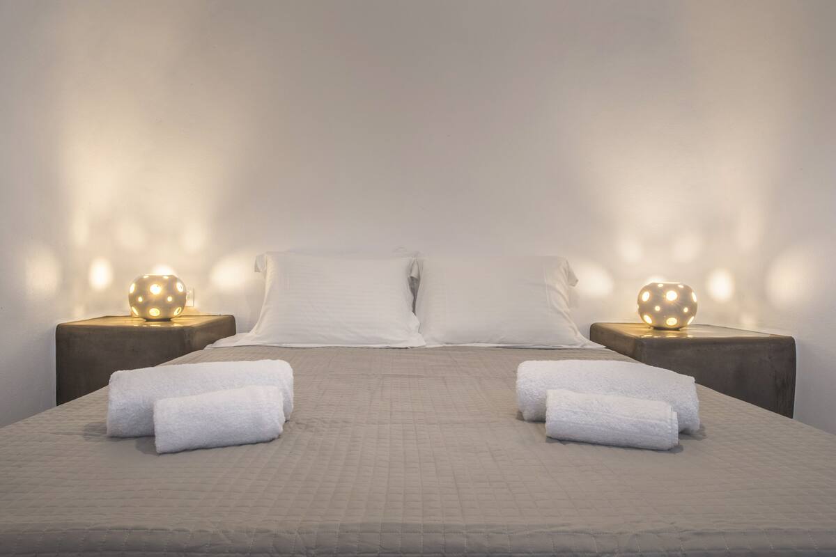 Una cama bien hecha con sábanas blancas y dos lámparas de noche con bases esféricas.