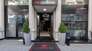 The entrance of the Conjores Hotel with a modern design, featuring a glass door, a black entrance, and a red logo on the doormat. - Confores Hotel (Istanbul)