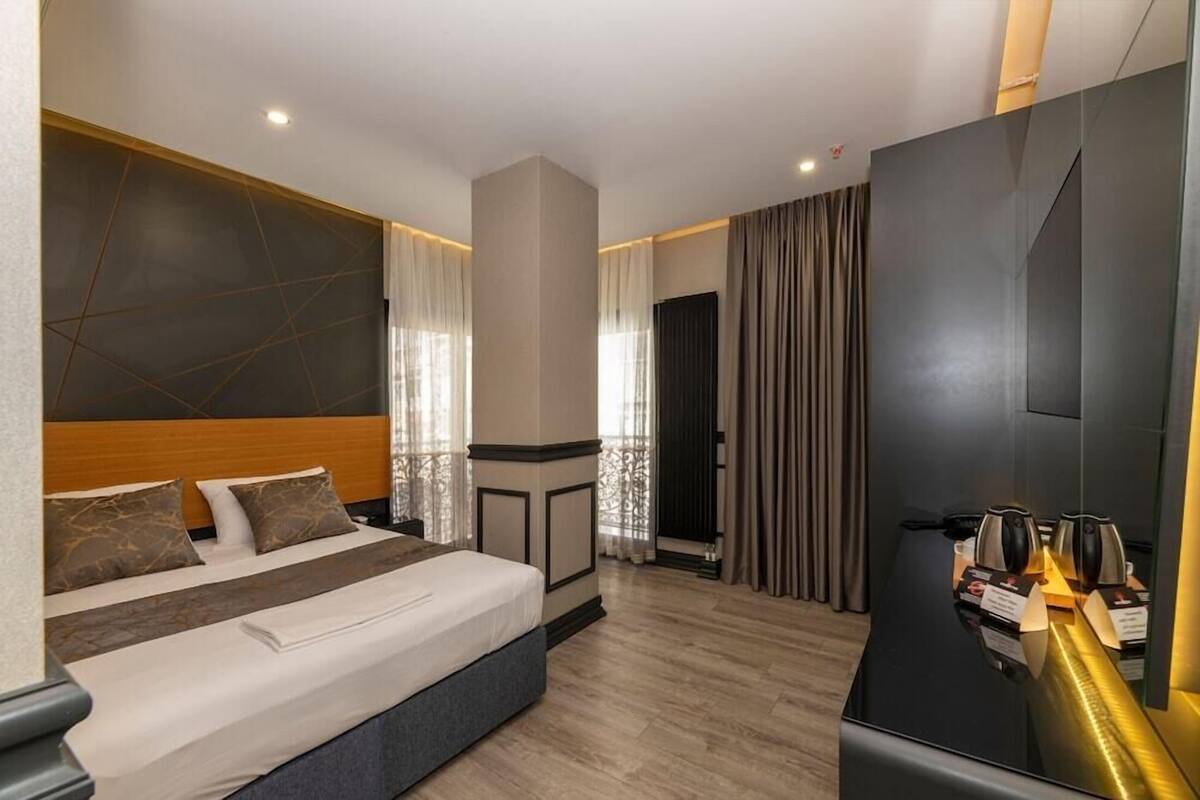 A modern hotel room with a large bed, a flat-screen TV, a coffee machine, and a small table.