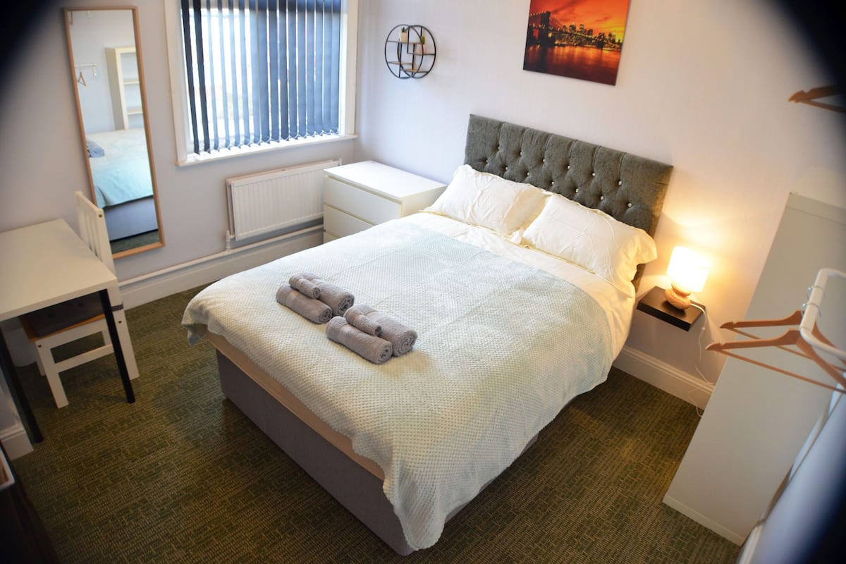 Un dormitorio ordenado con cama, mesita de noche y espejo.