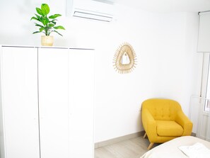 A room with a white wardrobe, a yellow armchair, a decorative wall piece, and a potted plant.