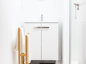 A white bathroom with a wooden towel rack, a white cabinet, and a door with a handle.