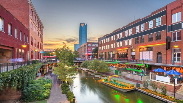 Escena urbana a orillas de un río, con edificios, un barco y un rascacielos moderno.